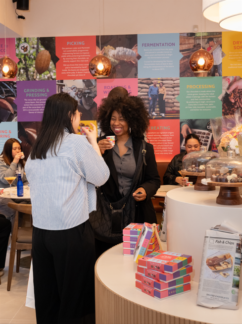 Two women interacting in a casual setting with a colorful wall display in the background.